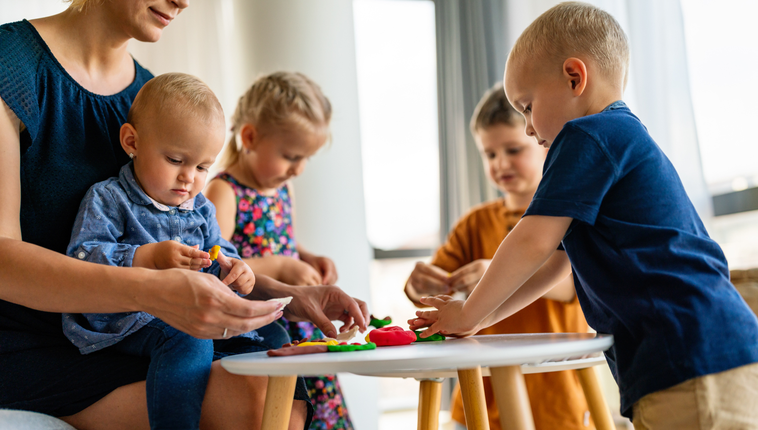 Mother or nursery teacher teaches her children to work with colorful play clay toys